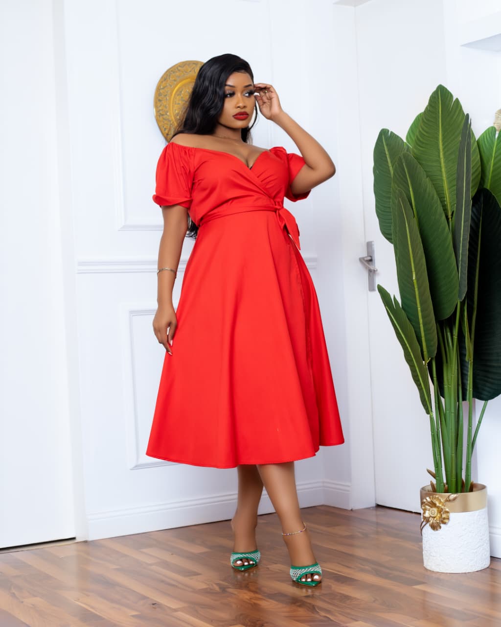 Woman in a red dress standing indoors with a plant in the background