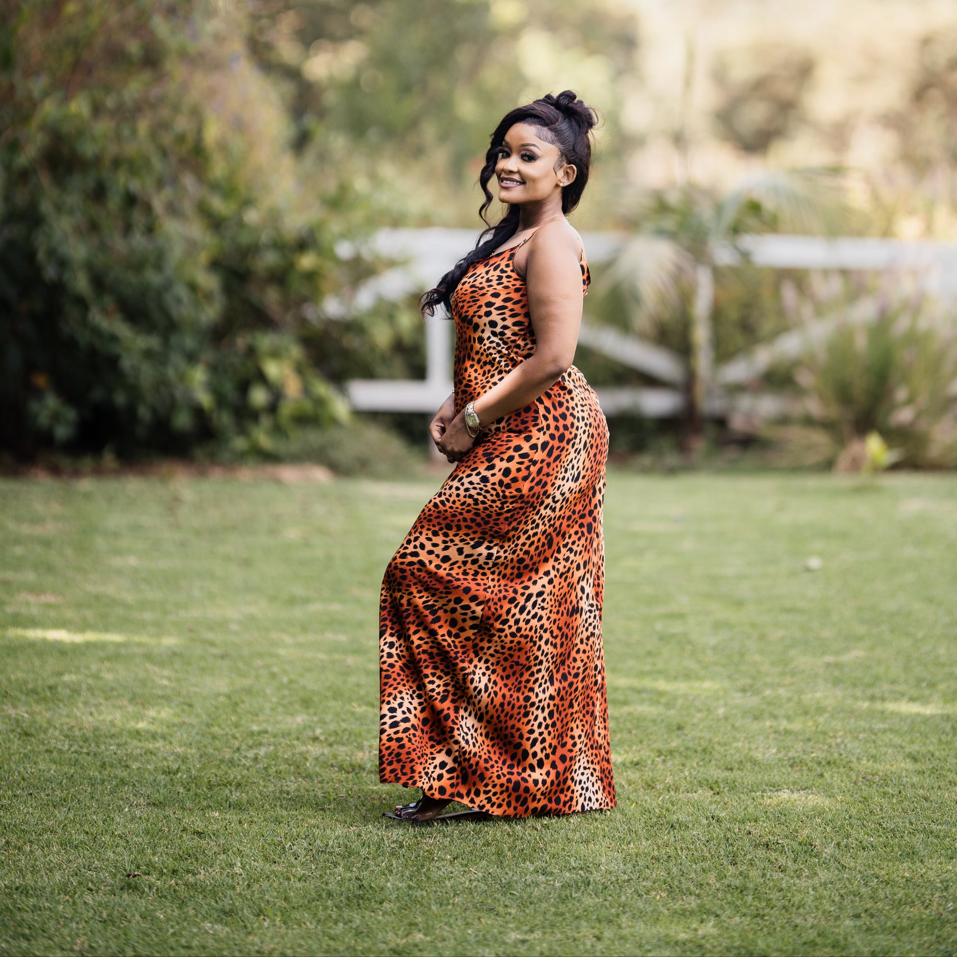 Woman in a leopard print dress standing in a grassy field with trees in the background