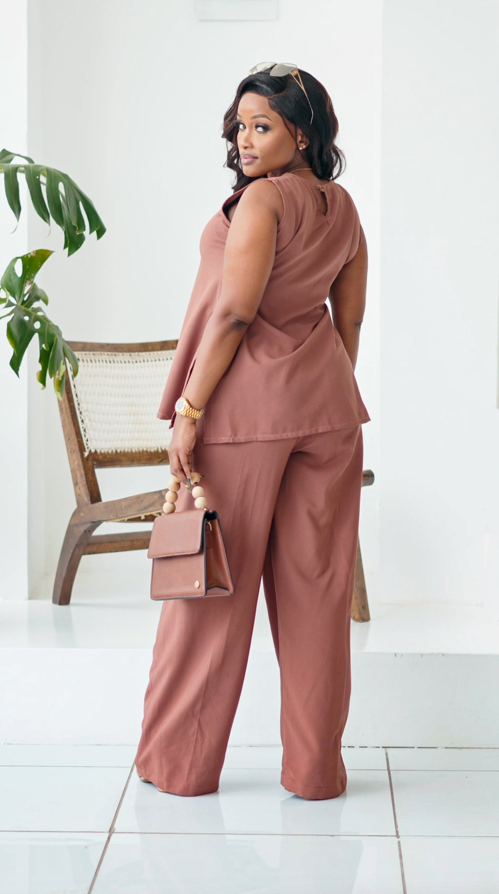 Woman in a pink outfit holding a matching handbag in a minimalistic setting.
