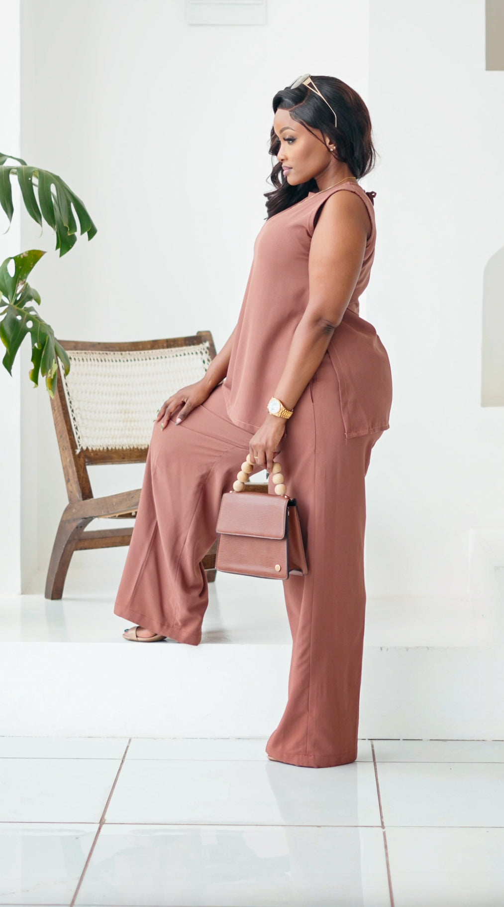 Woman in a pink jumpsuit holding a handbag in a minimalistic setting