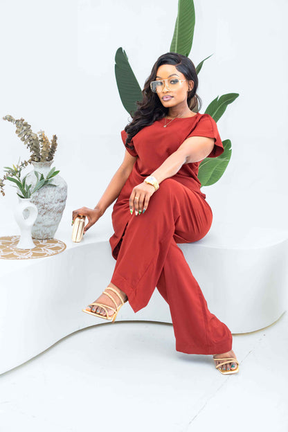 Woman in a red outfit sitting on a white chair with green leaves and a plant in the background