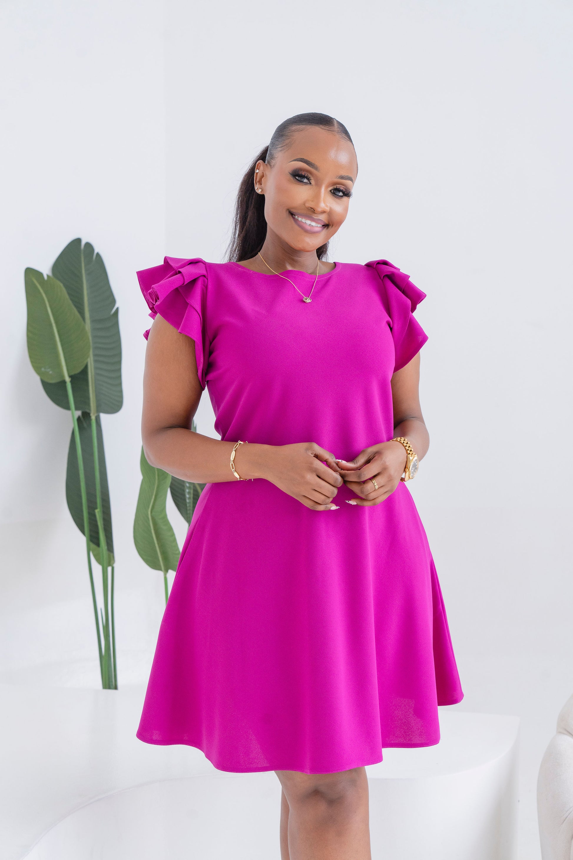 Woman wearing a bright pink dress with ruffled sleeves against a white background